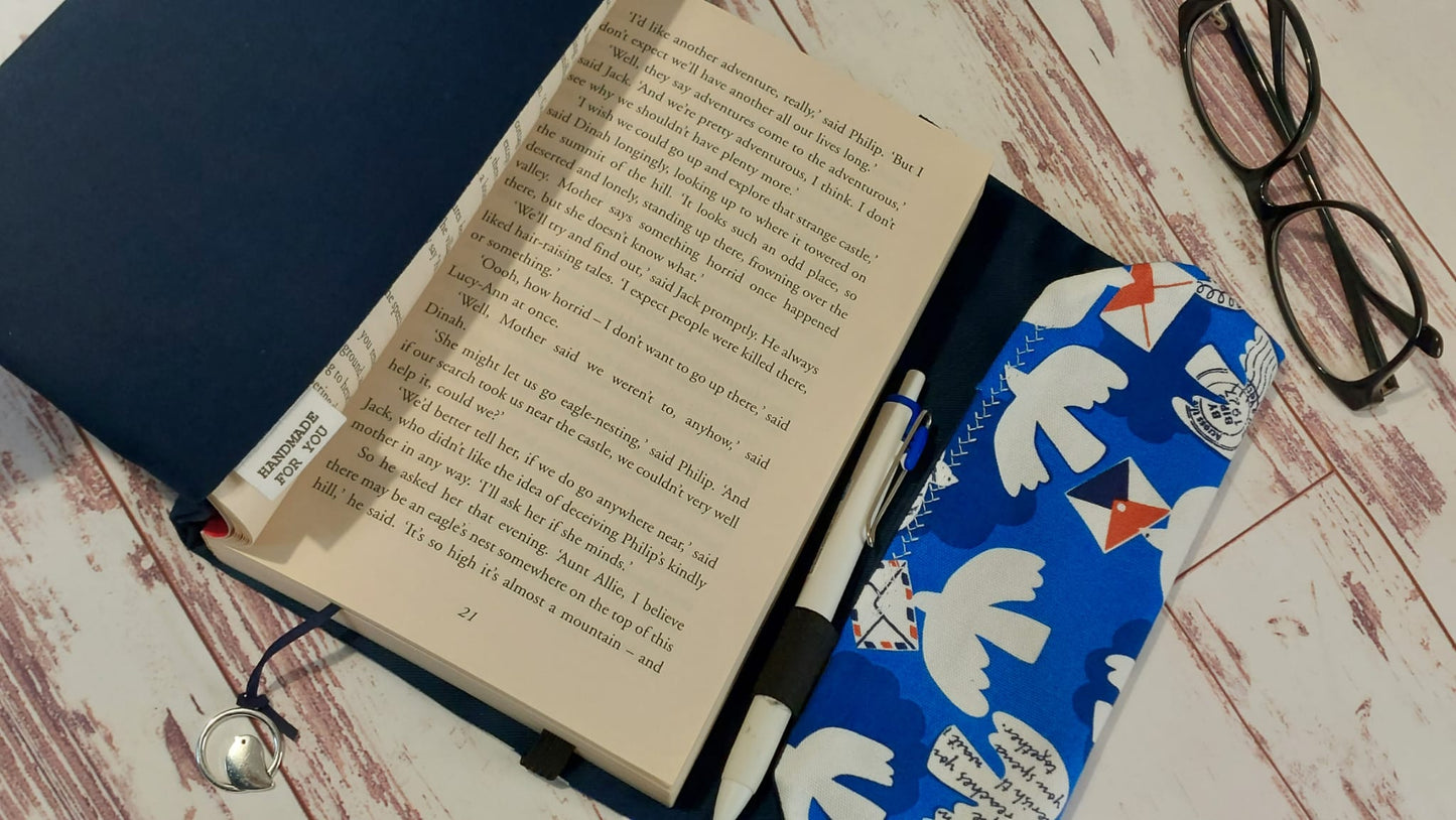 Handmade fabric book sleeve in navy blue with a blue, white, and red pattern featuring doves and envelopes, with a "Handmade for You" tag and a small metal bird bookmark charm.